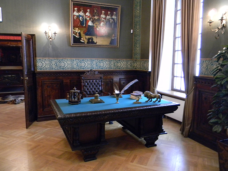 A big historical desk with pen and ink, a big painting in the background