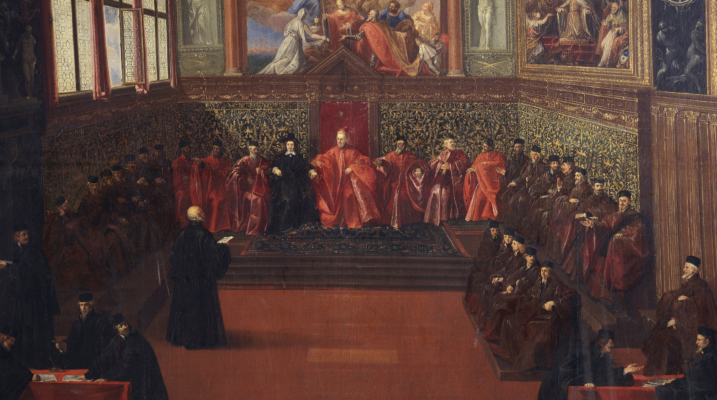 Officials in black and red robes sitting around the standing ambassador in a lushly decorated hall